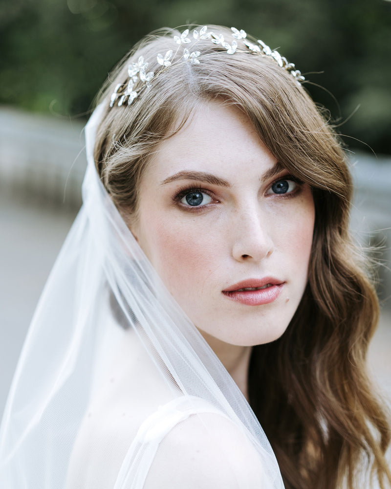 A model poses wearing a delicate crystal blossom hair vine in soft bridal waves. She is also wearing a soft tulle veil.