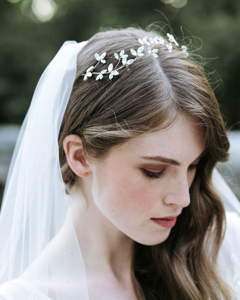 A model poses wearing a delicate crystal blossom hair vine in soft bridal waves. She is also wearing a soft tulle veil.