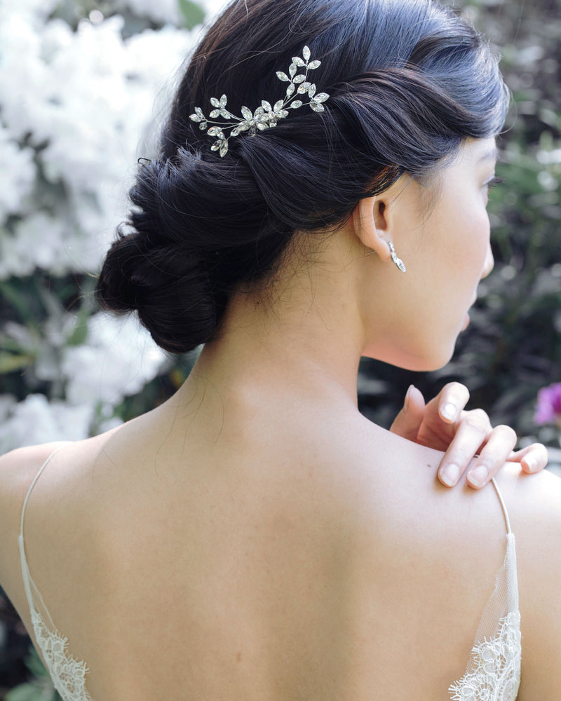 A dark-haired model with a low bridal updo is wearing a crystal bridal comb made of crystal leaf clusters.