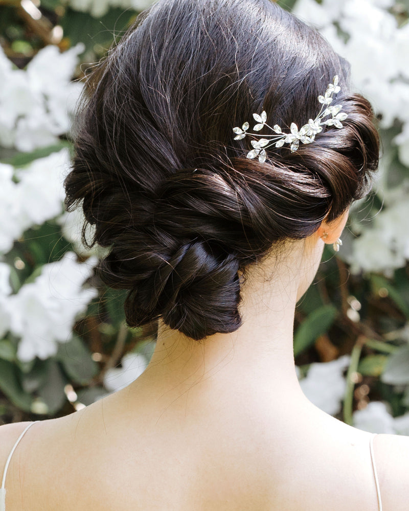 A dark-haired model with a low bridal updo is wearing a crystal bridal comb made of crystal leaf clusters in the side of her updo.