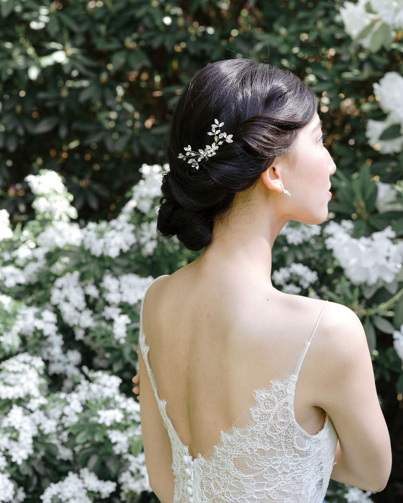 A dark-haired model with a low bridal updo is wearing a crystal bridal comb made of crystal leaf clusters, styled to the side.