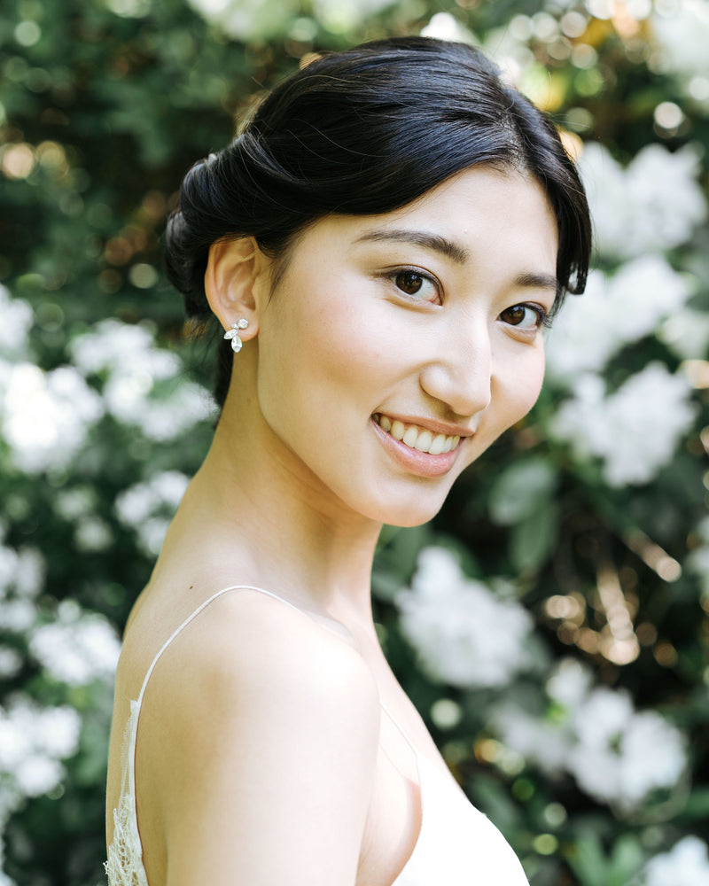 A model with dark hair styled in a low bridal updo smiles happily. She is wearing the Crystal Leaf Earrings in silver.