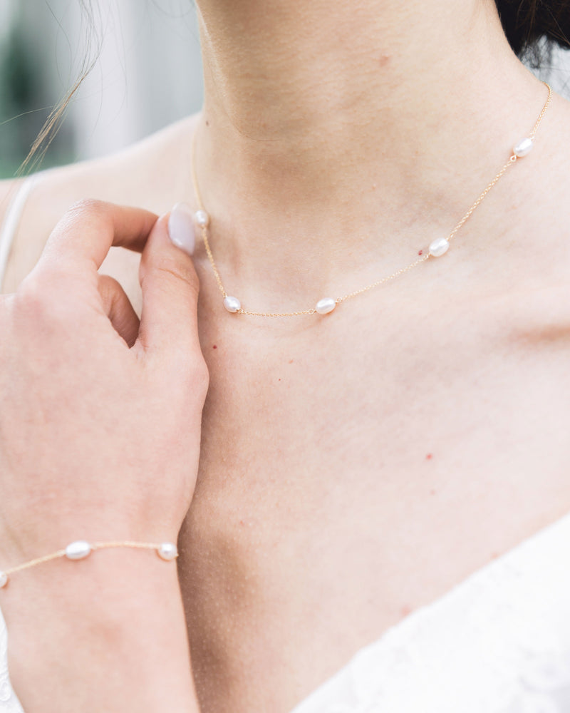 A close view of a model wearing the dainty freshwater pearl bracelet in gold with matching dainty pearl necklace.