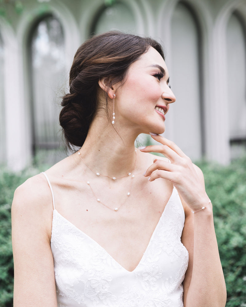 A model with a low bridal updo wears the Dainty Pearl Trio Earrings, paired with the Dainty Pearl Layered Necklace and Dainty Pearl Bracelet.