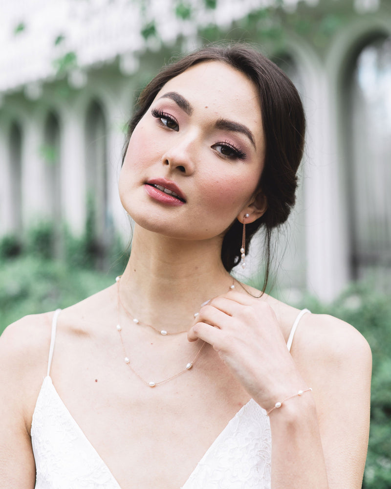 A model with a low bridal updo is wearing the Dainty Pearl Trio Earrings, paired with the Dainty Pearl Layered Necklace and Dainty Pearl Bracelet.