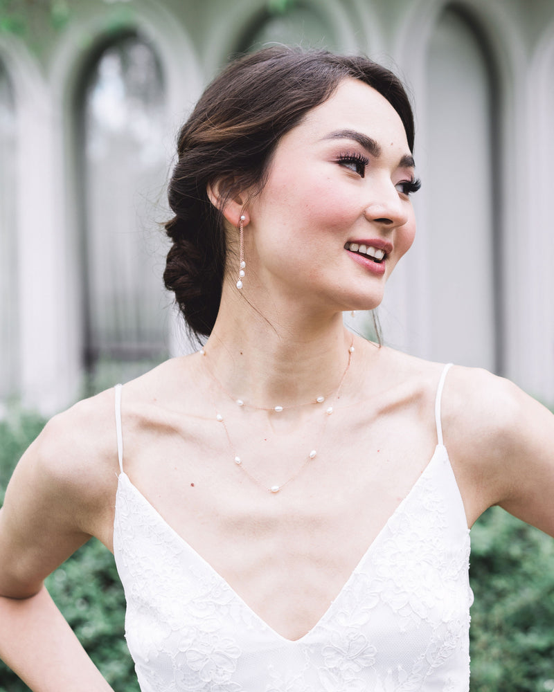 A model wears rose gold bridal jewelry; dainty pearl drop earrings, with a matching layered pearl necklace.