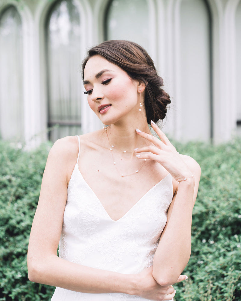 A model wears rose gold bridal jewelry; dainty pearl drop earrings, with a matching layered pearl necklace and dainty pearl bracelet.