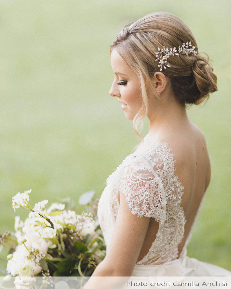 A model holds a romantic bouquet and is wearing a set of two delicate combs with freshwater pearl flowers and crystals styled into her low updo.