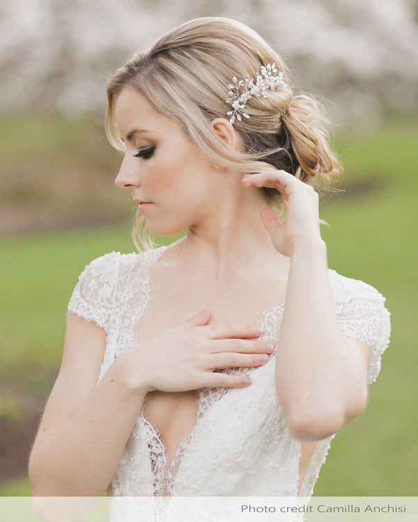 A model wears a set of two delicate combs with freshwater pearl flowers and crystals styled into her low updo.