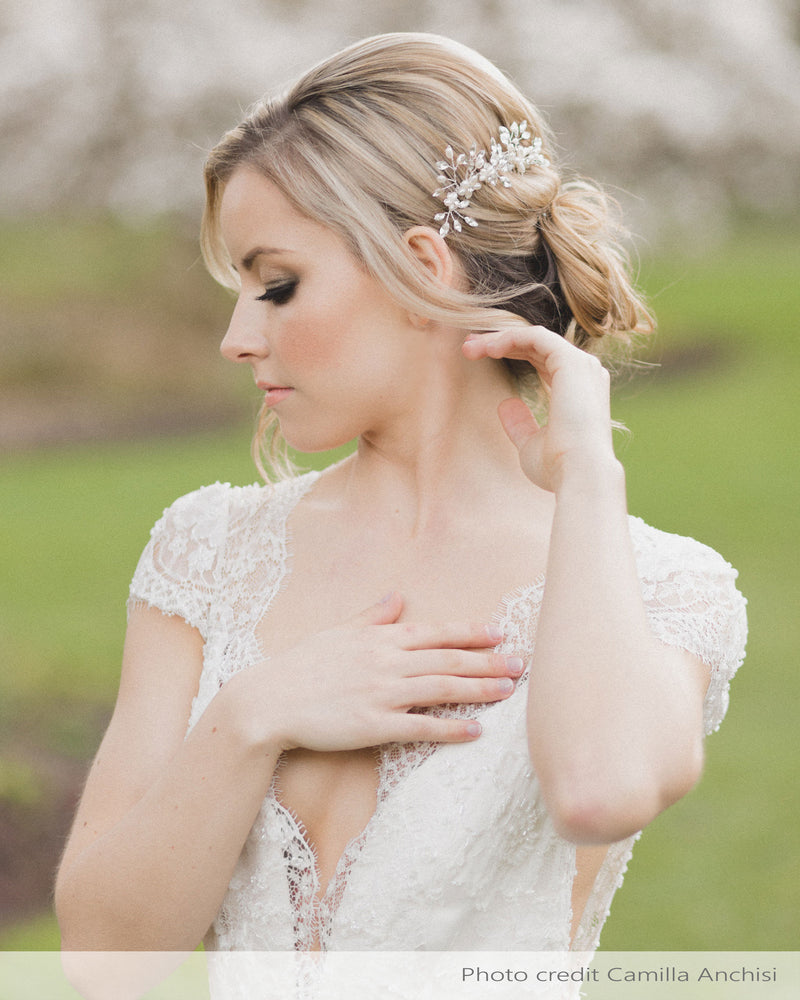 A model wears a set of two delicate combs with freshwater pearl flowers and crystals styled into her low updo.