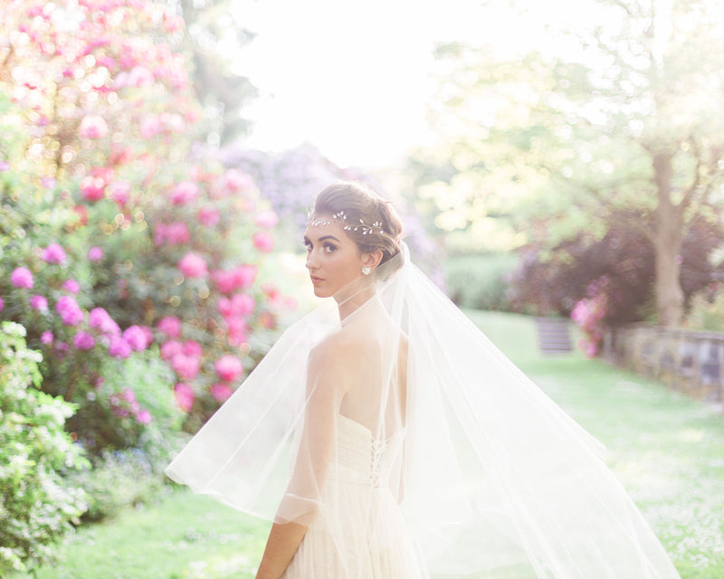 A model poses at golden hour at Aberthau Mansion. The two-layer Delphine Veil is styled with its blusher to the back and the tulle floats softly as she turns.