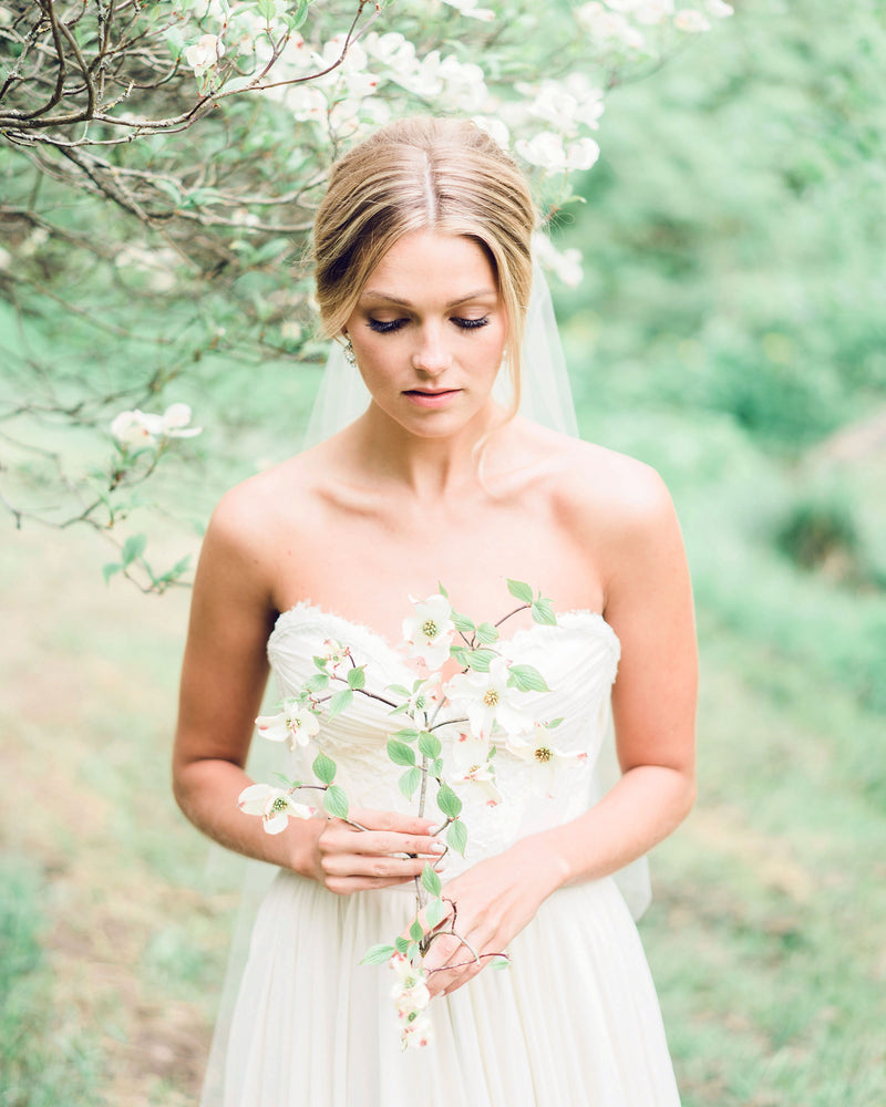 A model holds wildflowers in her hands. Our Delphine Gathered Veil is styled into her romantic bridal updo.