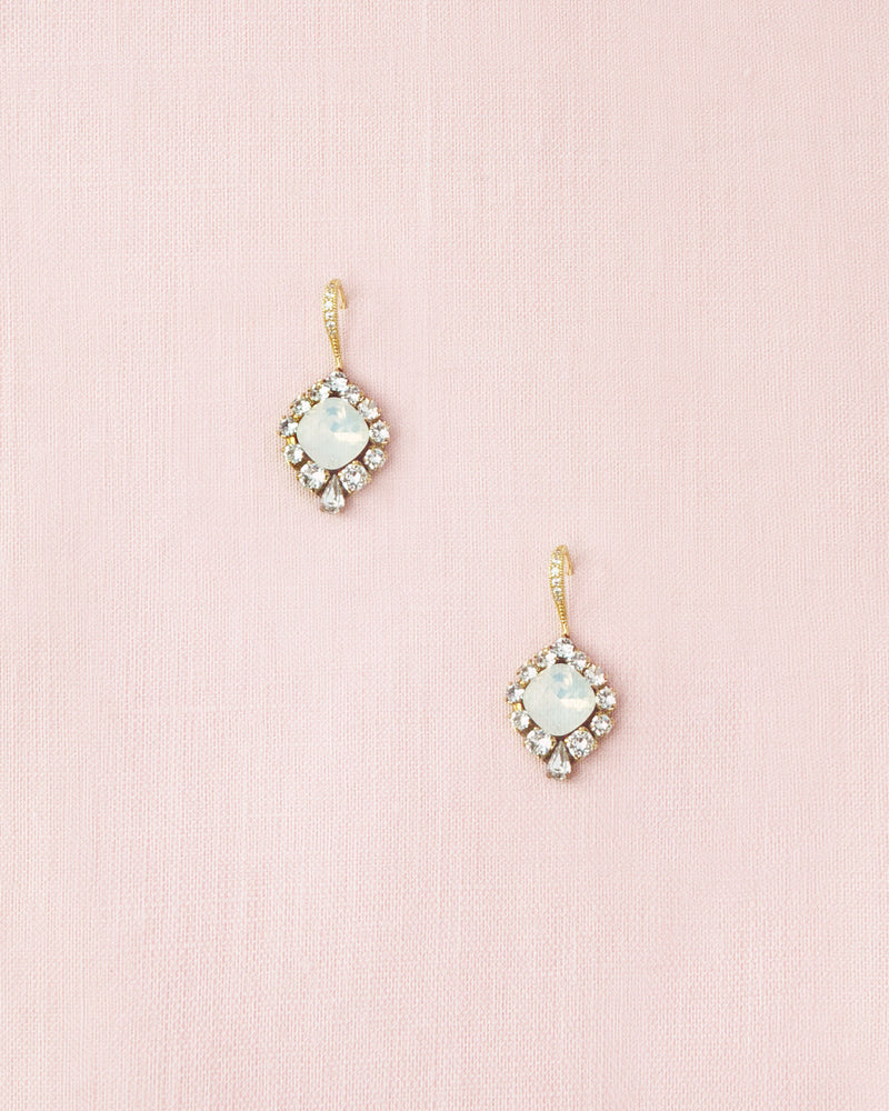 Flatlay of the Enchanted Crystal Drop Earrings in gold with white opal crystal centers. The pave crystal hook version is shown.