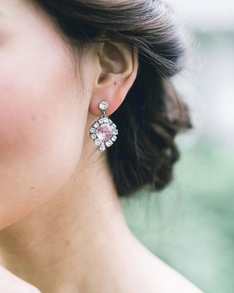 A close model view of a bride wearing the Enchanted Crystal Drop Earrings in silver with blush crystal centers. 