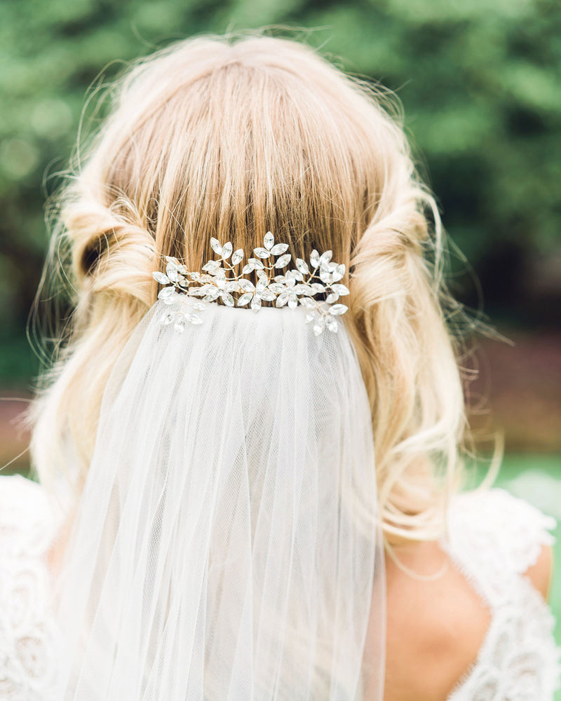 A model wears her hair styled down with soft waves and pieces on both sides pinned up. She wears the Enchanted Crystal Bridal Comb in the back, over a veil.