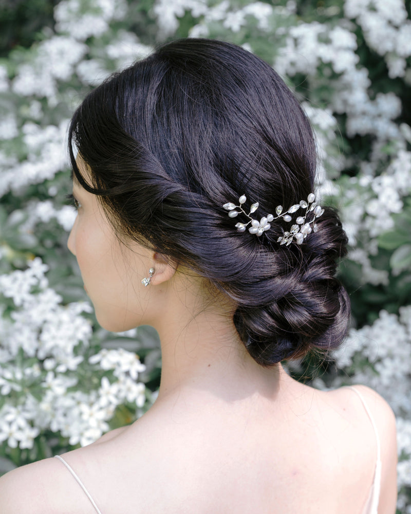 A model has her dark hair styled into a low bridal updo with twists and a braided knot. The Everthine Pearl & Crystal Hair Pins are styled into the back of her updo, slightly to the side.