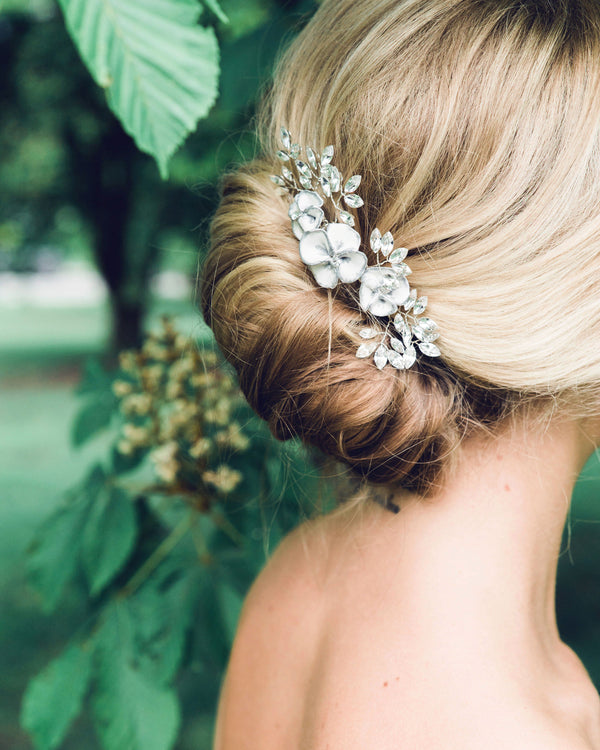 Close model view of the Gilded Blossoms Comb styled into a modern bridal French twist. The comb has white flowers with silver edges, pearls and crystals.