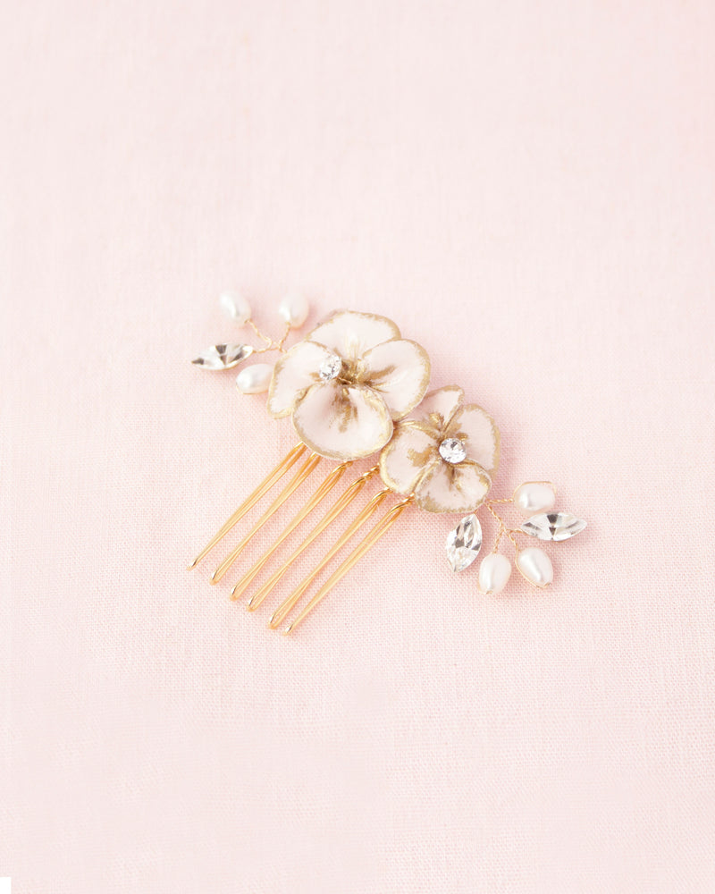 Flatlay on a pink background of a small bridal comb with blush flowers with gold hand-painted edges, freshwater pearls and crystals