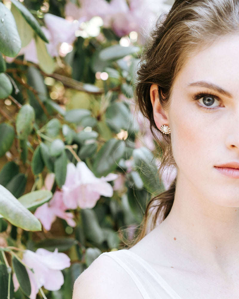 A model wears the Halo Pearl Stud Earrings in gold with cream pearls.