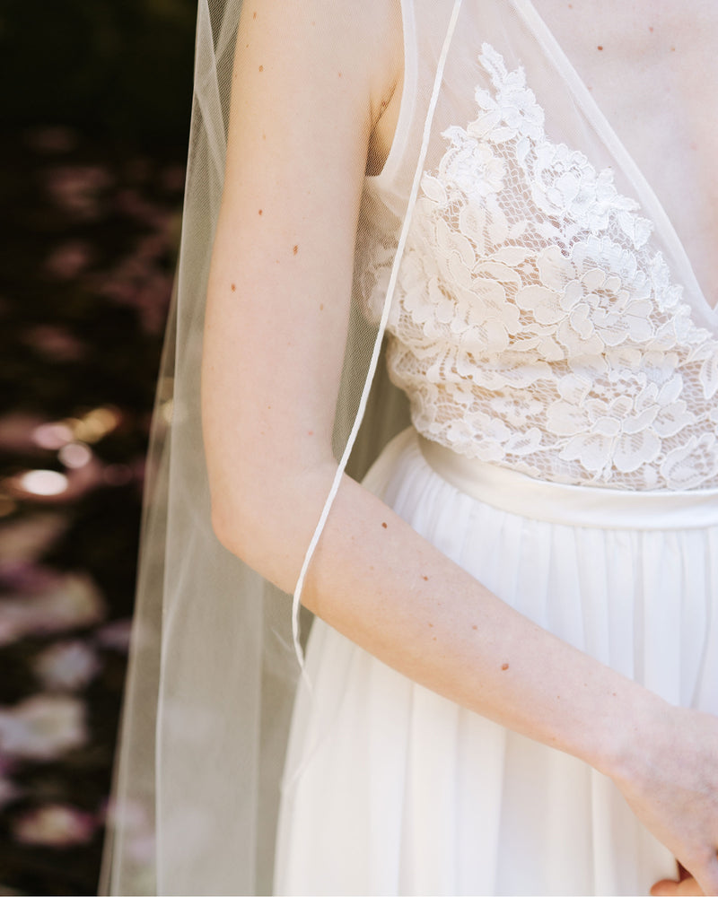 A bride wears a single layer veil with a delicate ribbon edge.