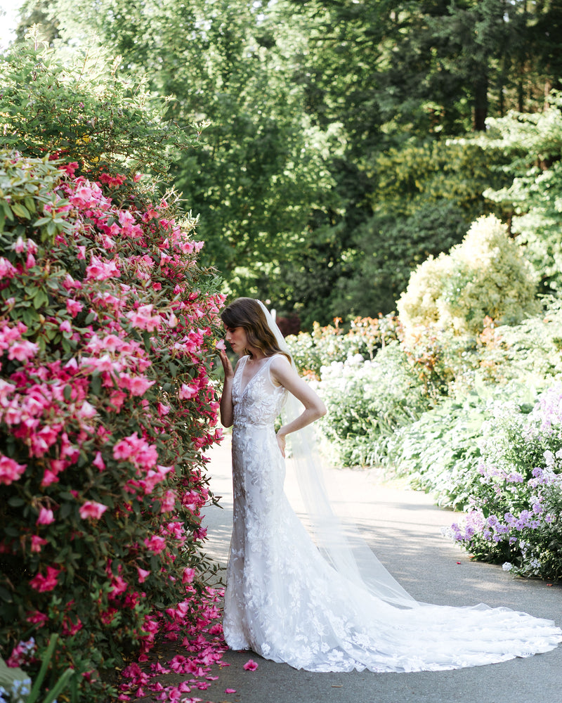 A bride stands in a flower garden. She wears a classic long veil with no trim.