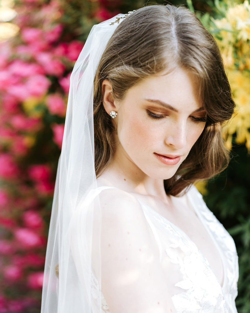 A bride with her hair styled down in soft waves wears a simple tulle veil without trim.