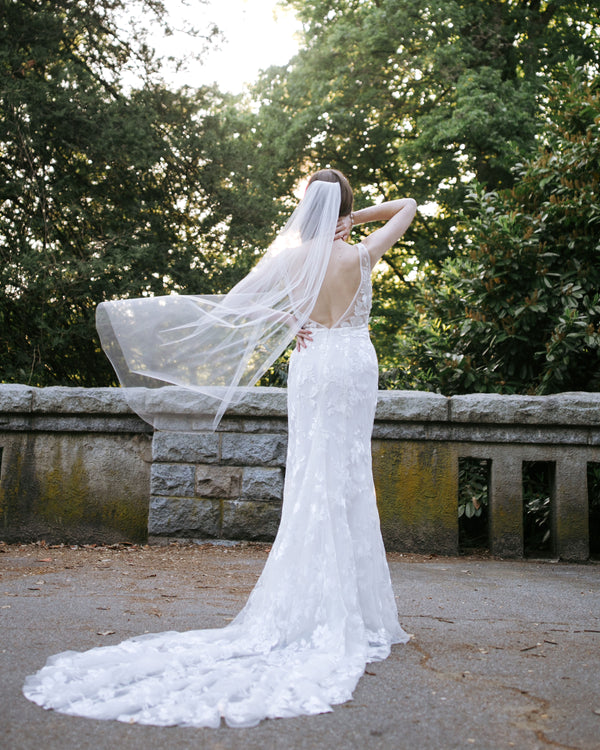 A bride wears a fingertip veil that floats in the air behind her; the veil is simple, with soft gathers and no edge.