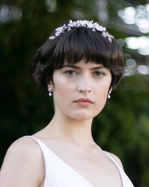 A bride with a pixie hairstyle wears the Lily Floral Crown in silver with pearl earrings.