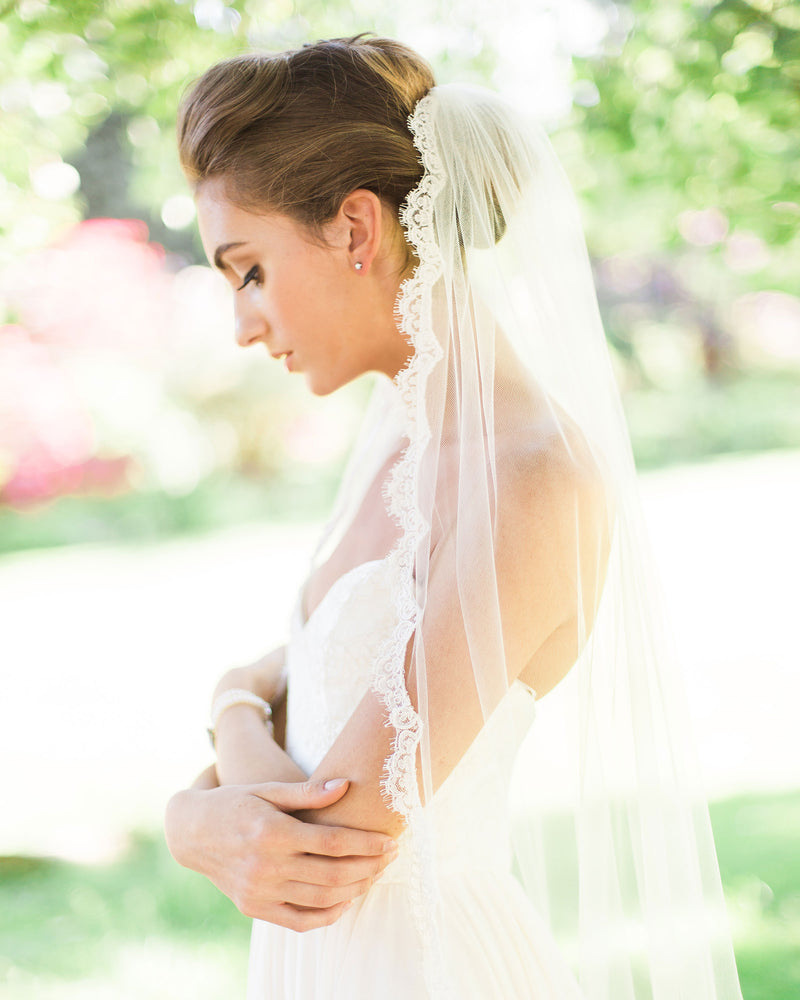A close side view of a model wearing the Magnolia Lace Veil in fingertip length.