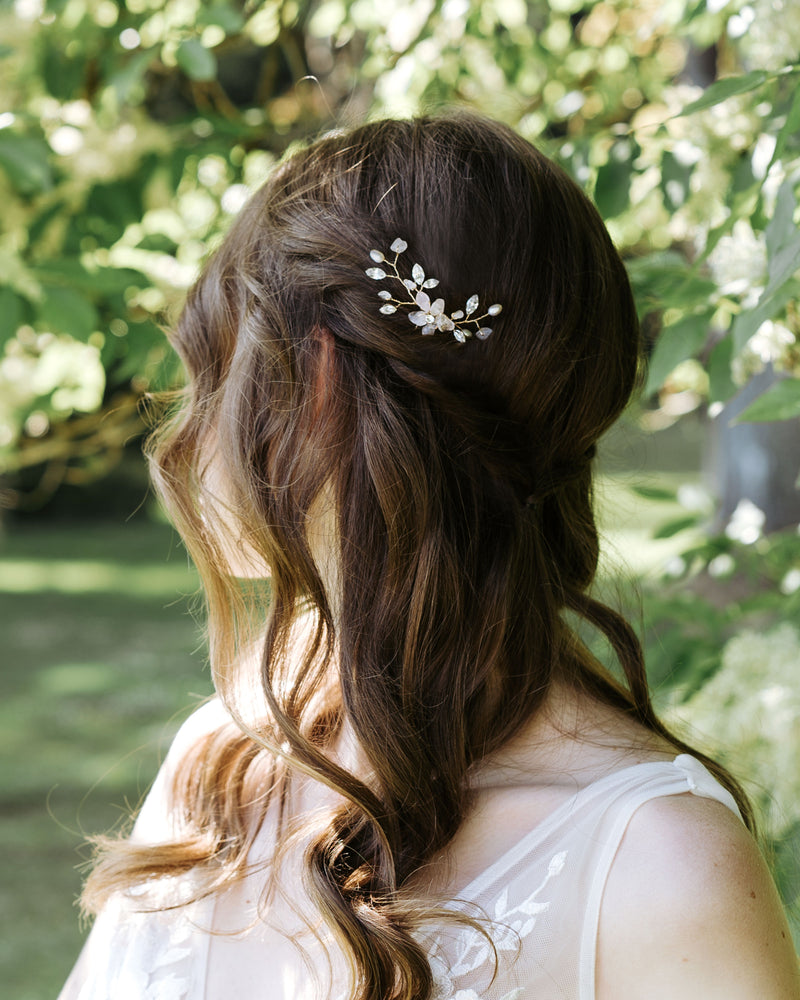 A bride whose hair is half-up with a relaxed braid wears the Moonflower Comb in gold, with rose quartz gemstones, pearls, and crystals.
