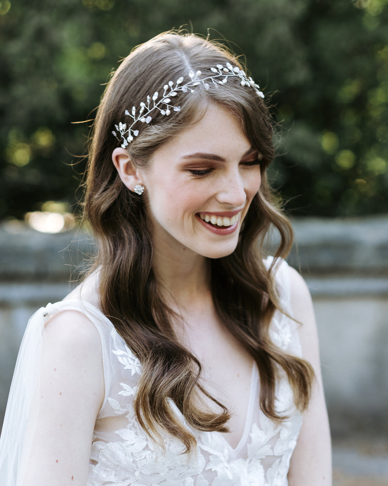 A bride wears a hair vine of scattered crystals, freshwater pearls, and moonstone. Her hair is styled in soft bridal waves.