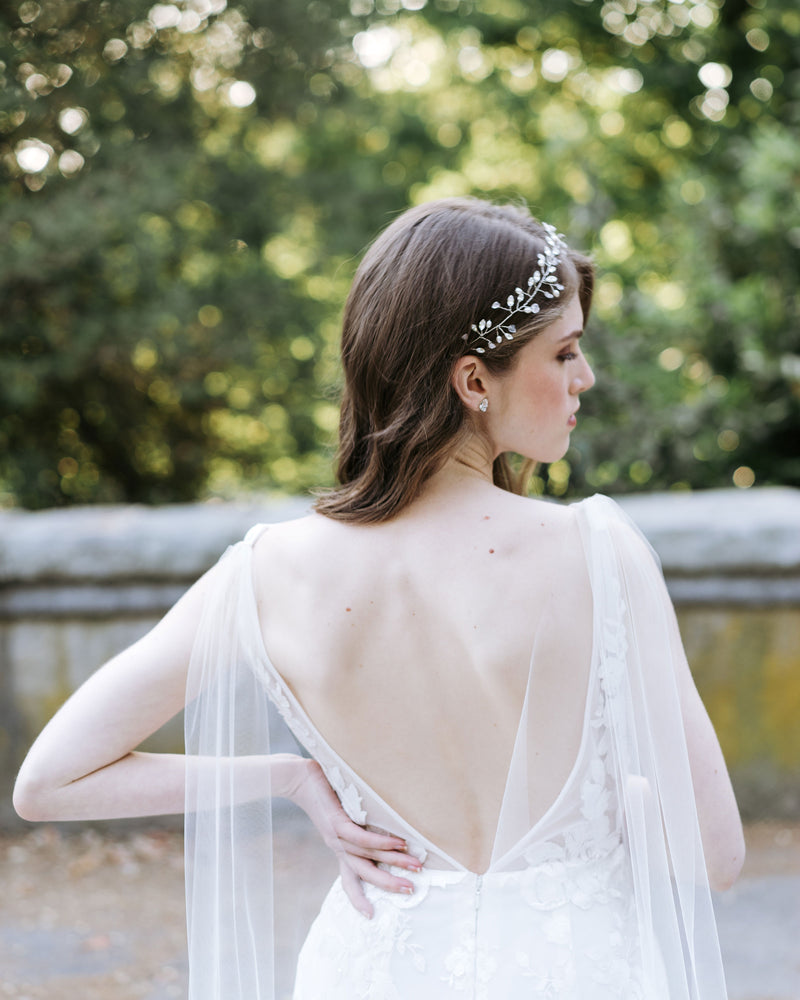 A bride wears a tulle cape veil, paired with crystal stud earrings and a bridal hair vine with pearls, crystals, and moonstone.