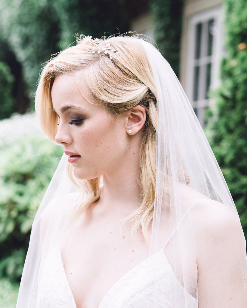A bride wears classic pearl stud earrings in petite size; paired with a floral bridal crown.