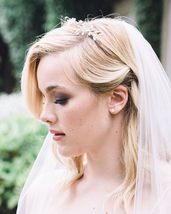 A bride wears classic pearl stud earrings in petite size; paired with a floral bridal crown.