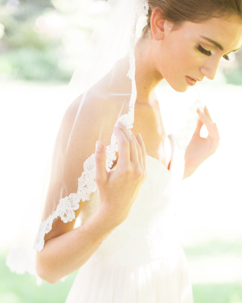 A bride wears a short veil with lace flower edge.