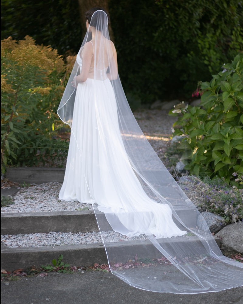 A bride wears the Primrose Ribbon Veil in cathedral length in light ivory.