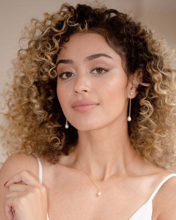A model wears a pearl jewelry set with 2" long pearl earrings and a matching teardrop necklace.