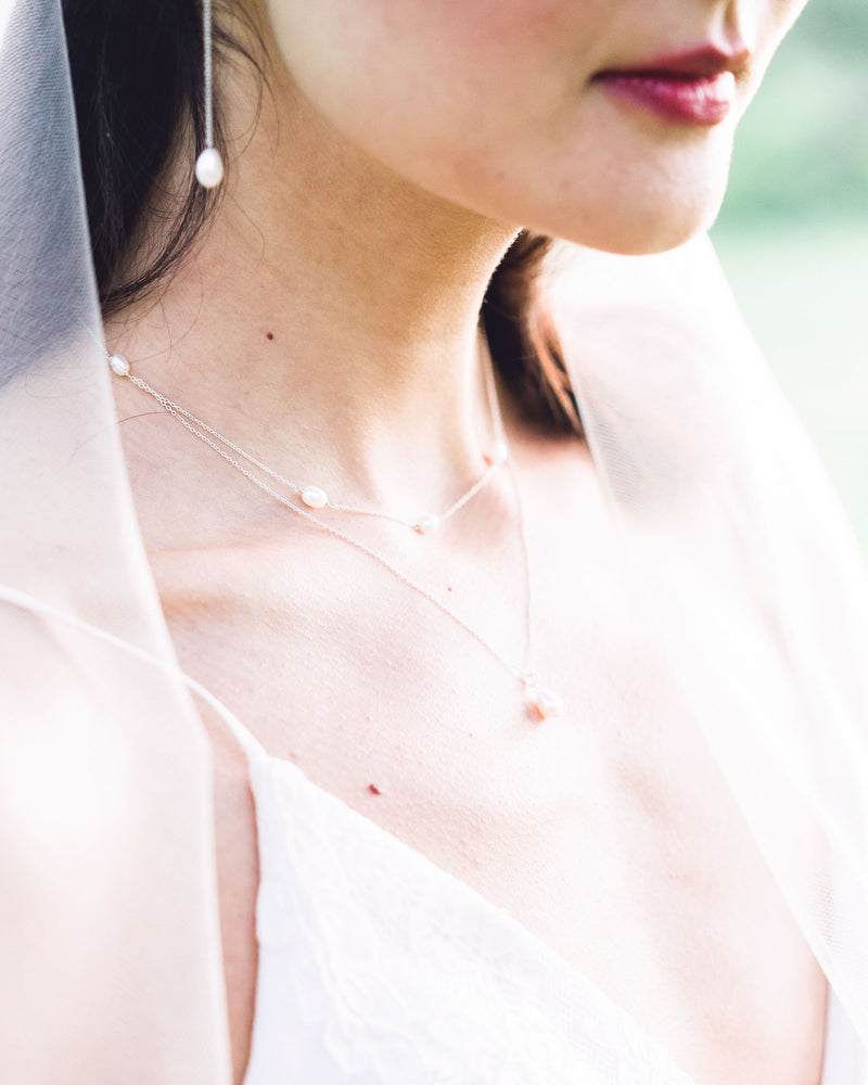 A bride wears a modern pearl jewelry set with Long Pearl Teardrop Earrings and a Layered Pearl Drop Necklace.