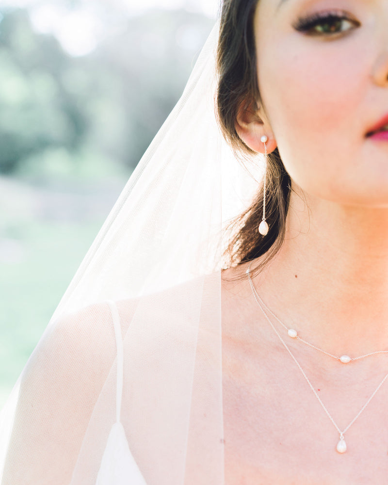 A bride wears a modern pearl jewelry set with Long Pearl Teardrop Earrings and a Layered Pearl Drop Necklace.