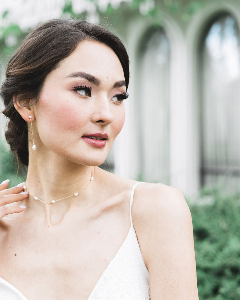 A bride wears Teardrop Pearl Long Earrings, paired with a pearl station necklace.