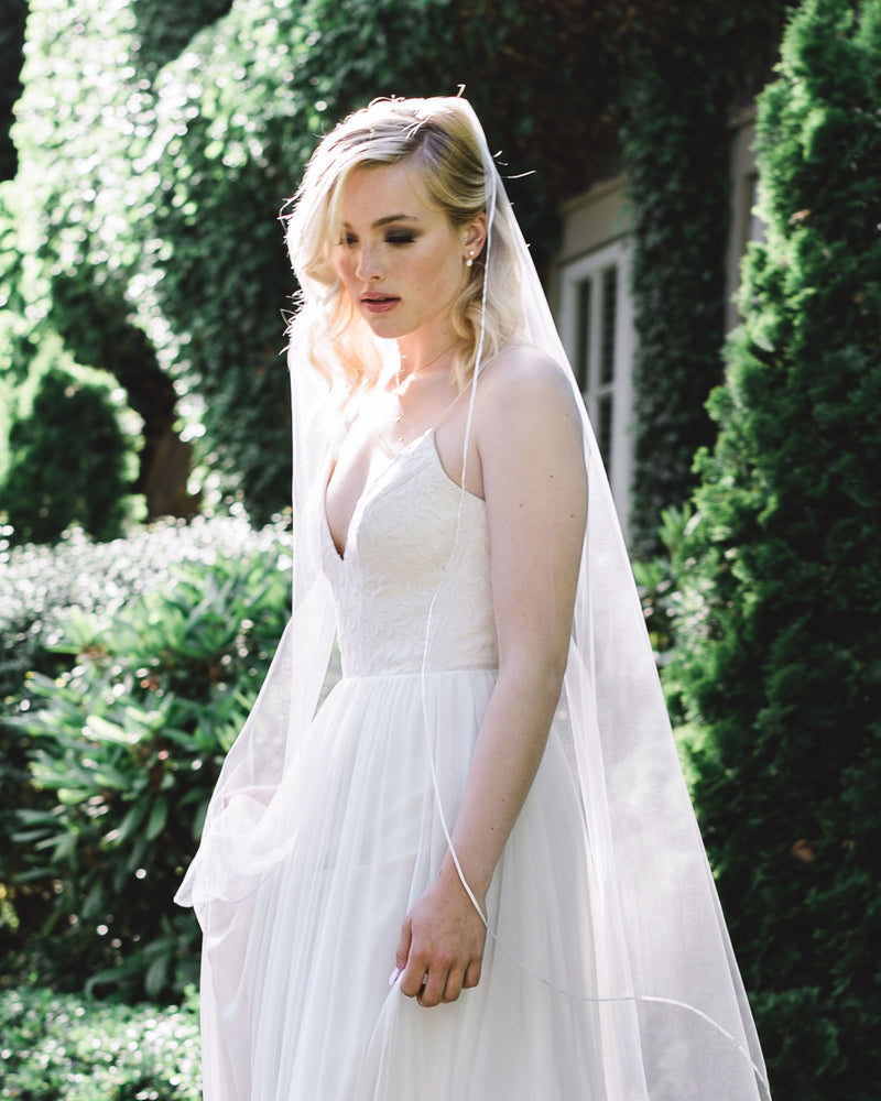 A bride wears classic Teardrop Pearl Drop Earrings with a ribbon trim veil without gathers.