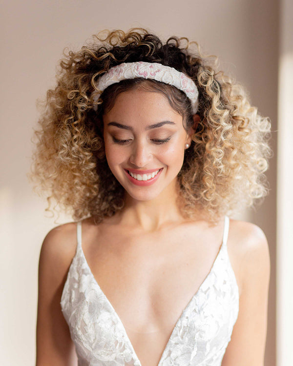 A model smiles wearing the Wildflower Padded Headband in blush/off white with matching blush pearl studs.