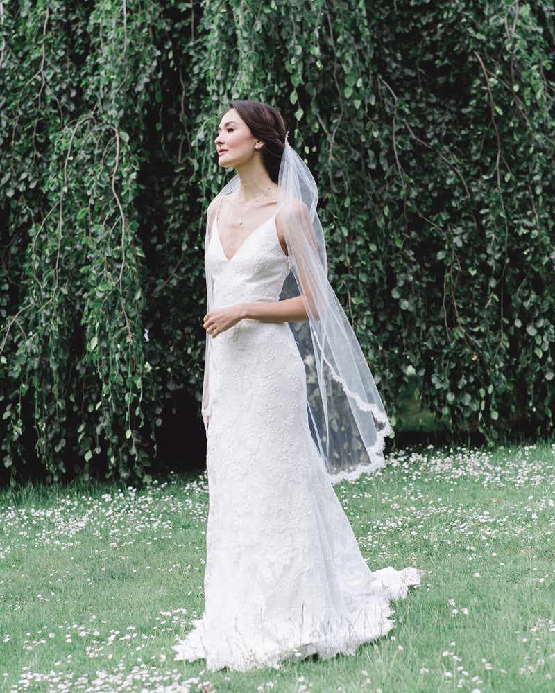A bride wears the Wisteria Lace Veil; a fingertip veil with lace starting at the elbow.